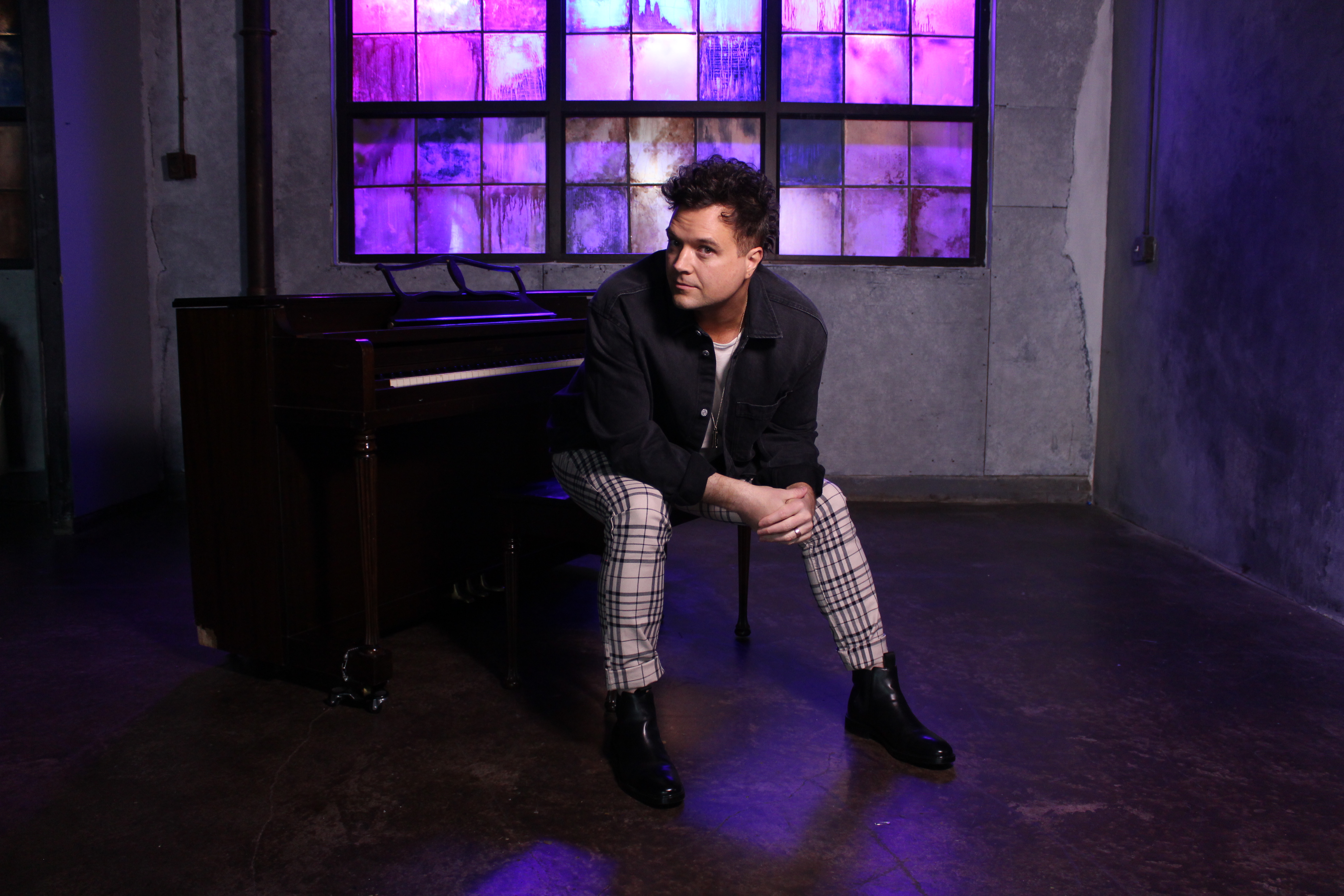 Nathan Walters seated by a piano in a cinematic studio setting